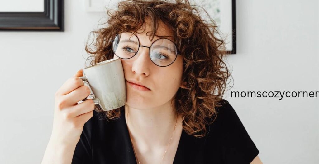A woman with curly hair and glasses looking pensive while holding a coffee mug, capturing a moment of overthinking.